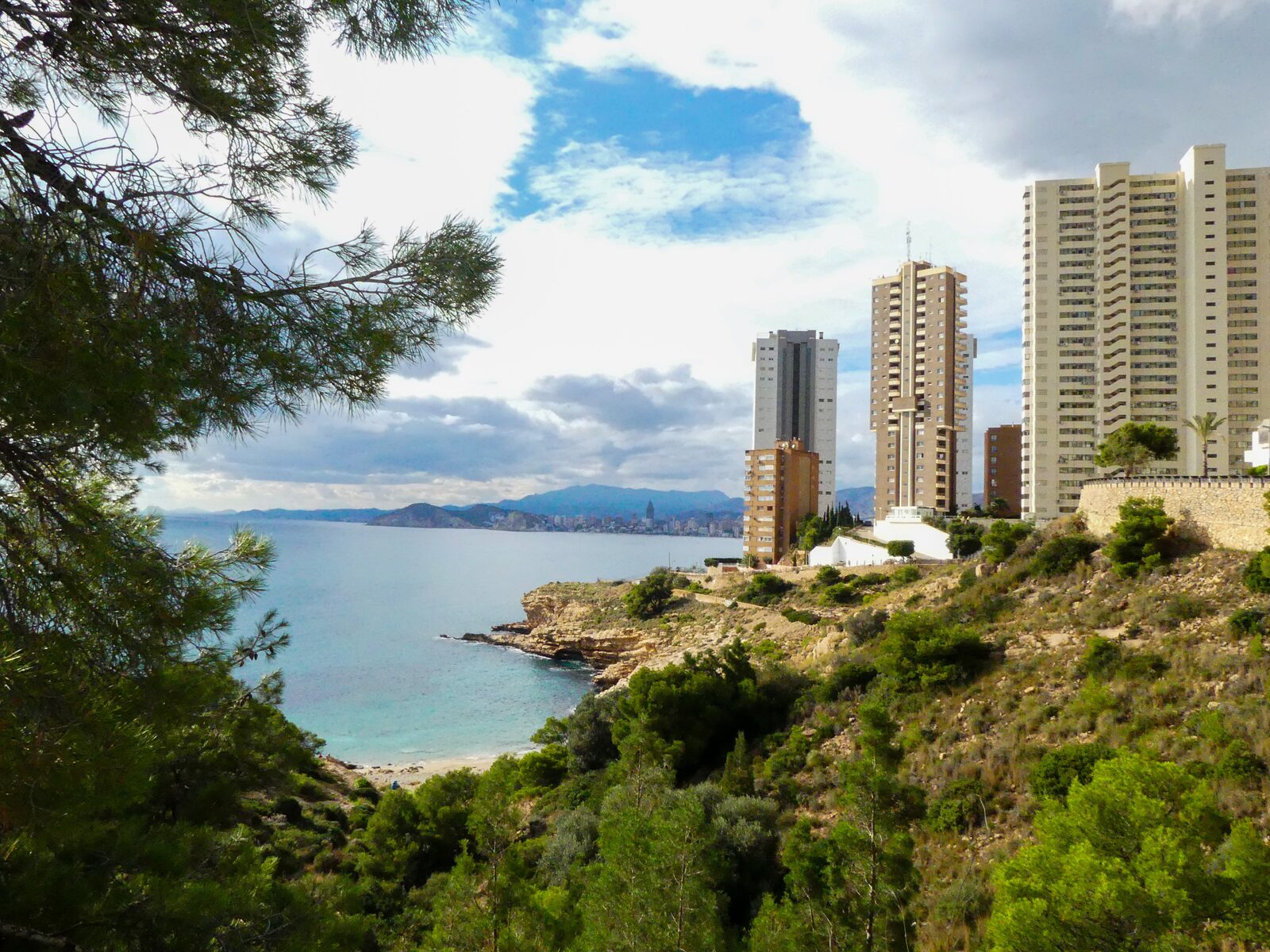 Uitzicht langs de bomen op de skyline van Benidorm vanaf Cala Almadraba