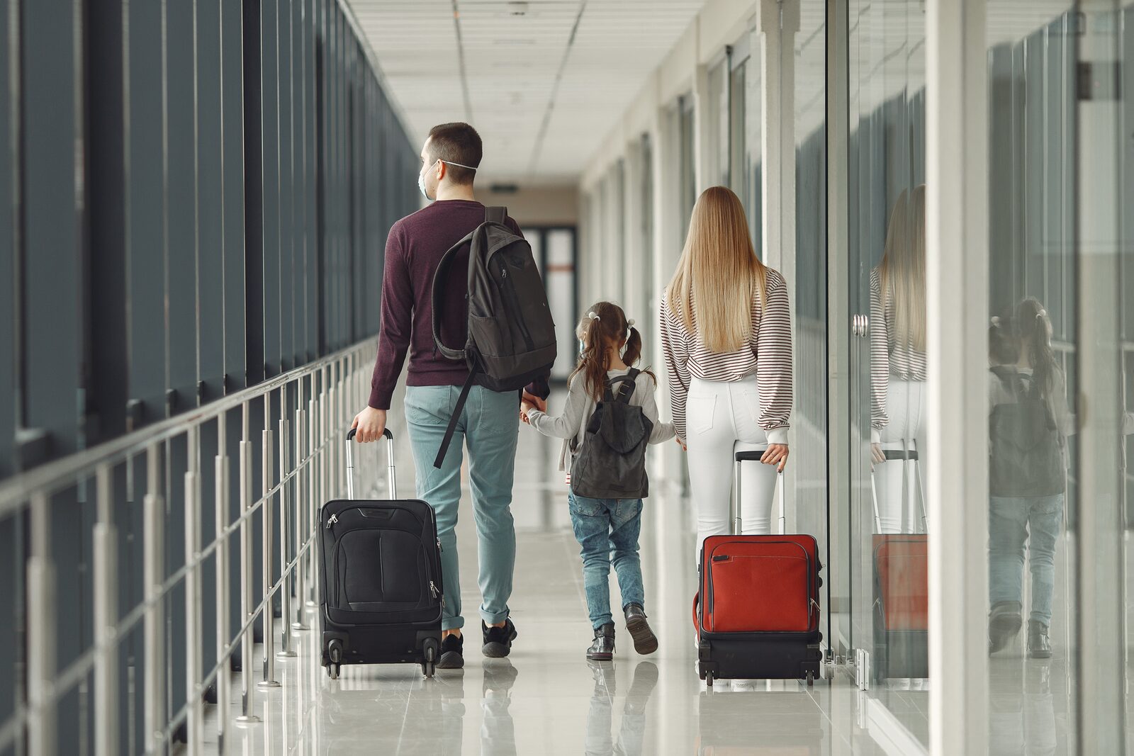 Gezin met rolkoffers en mondkapjes lopen op de luchthaven 