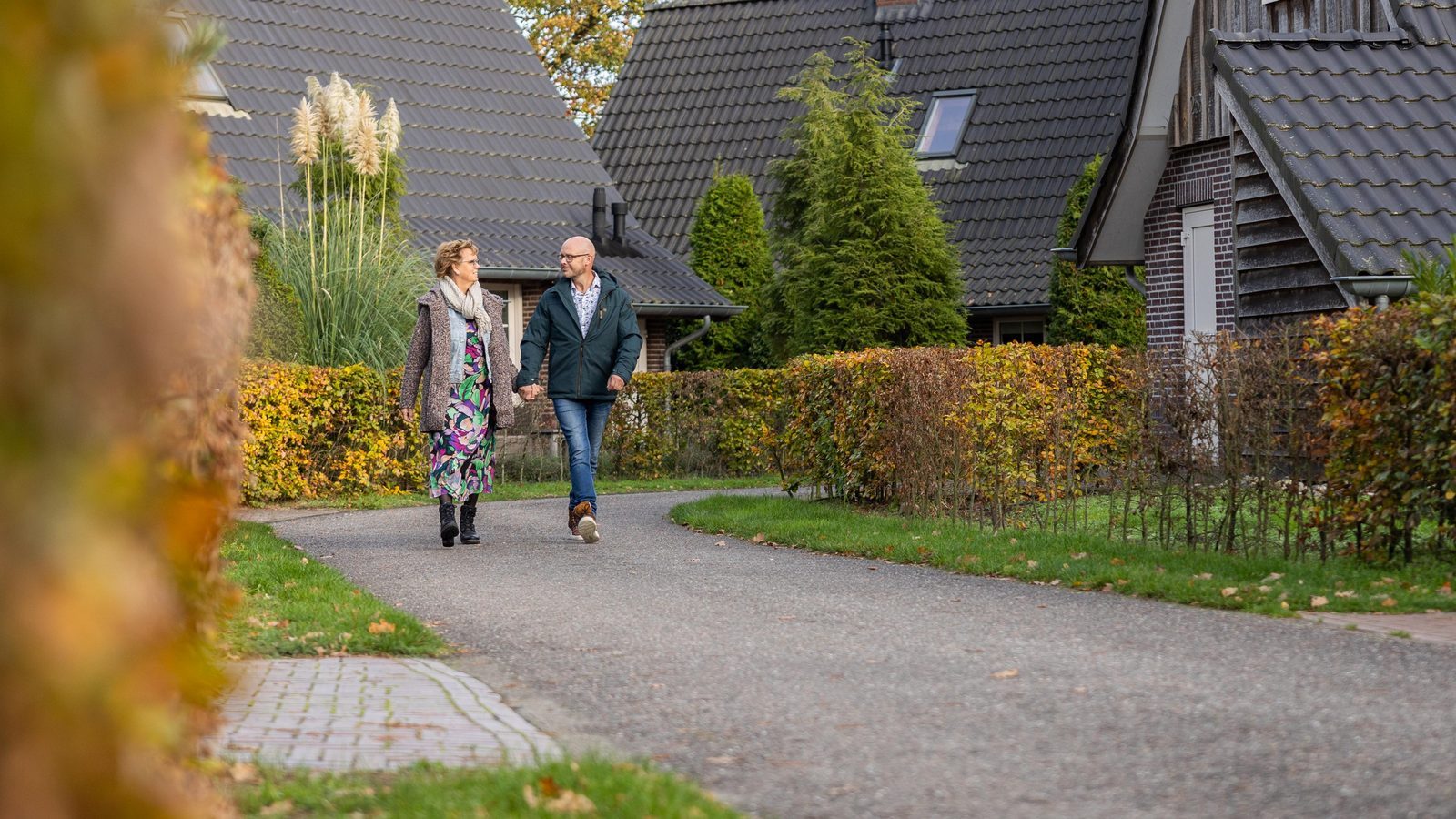 Ein Paar spaziert durch die herbstliche Natur und an den Häusern des Villaparks Hof van Salland vorbei