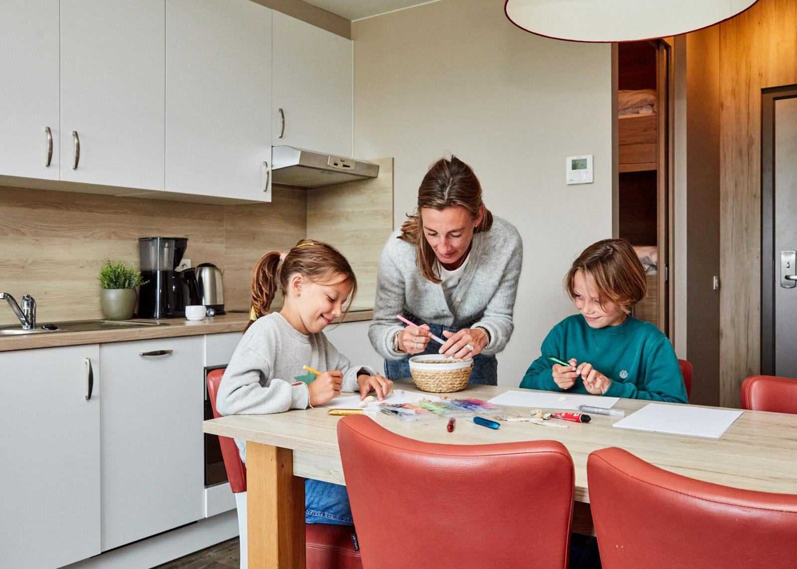 Een mama met haar kindjes aan het knutselen in een vakantieappartement van Holiday Suites