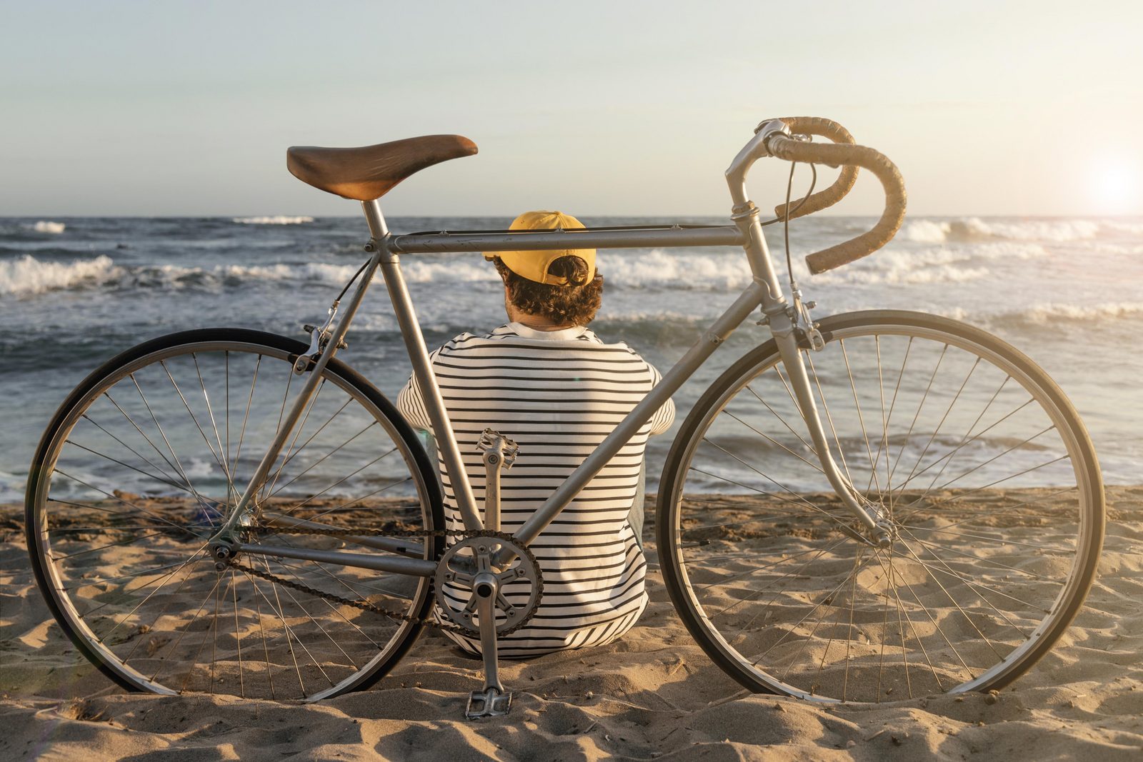 Hombre sentado en la playa con una bicicleta de carreras mirando al mar