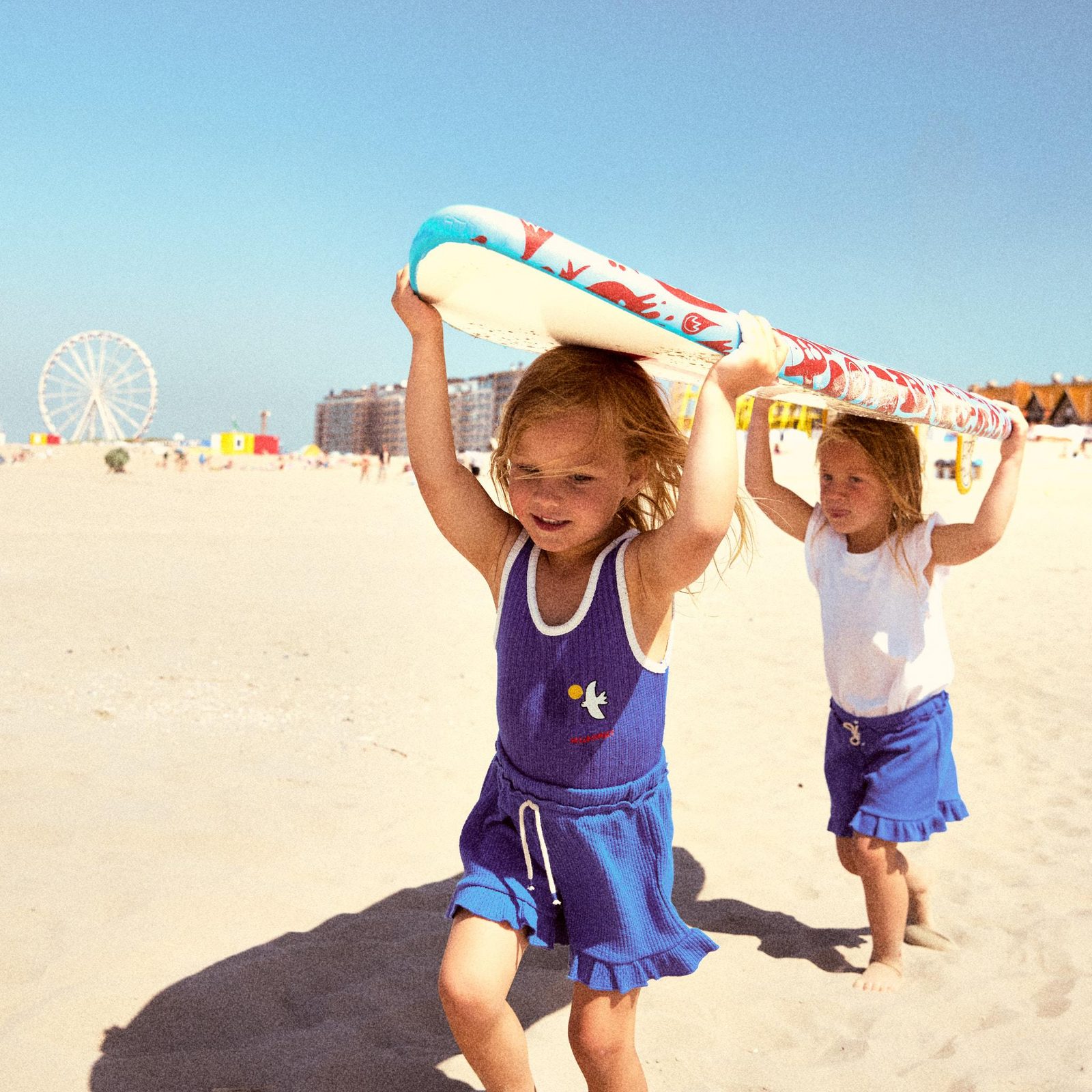 2 meisjes die een surfboard boven hun hoofd dragen