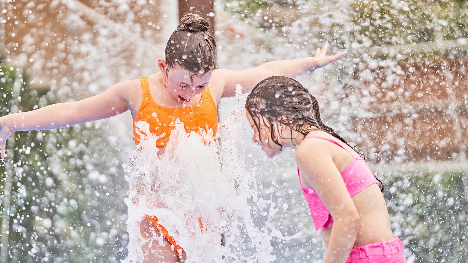 Two girls having fun getting sprayed by water and smiling at Woolacombe Bay Holiday Park outdoor fun pool