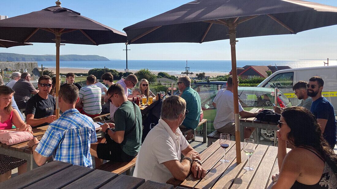 People enjoying the sun under a parasol with a sea view, drinking beer and wine.