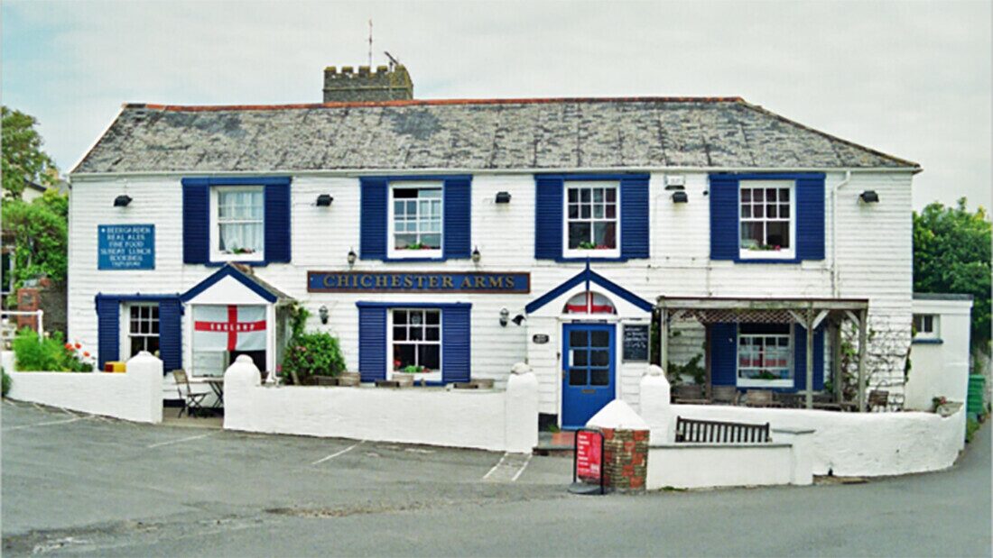 Front view of the Chichester Arms pub, a traditional white building with blue shutters and a welcoming entrance in North Devon.