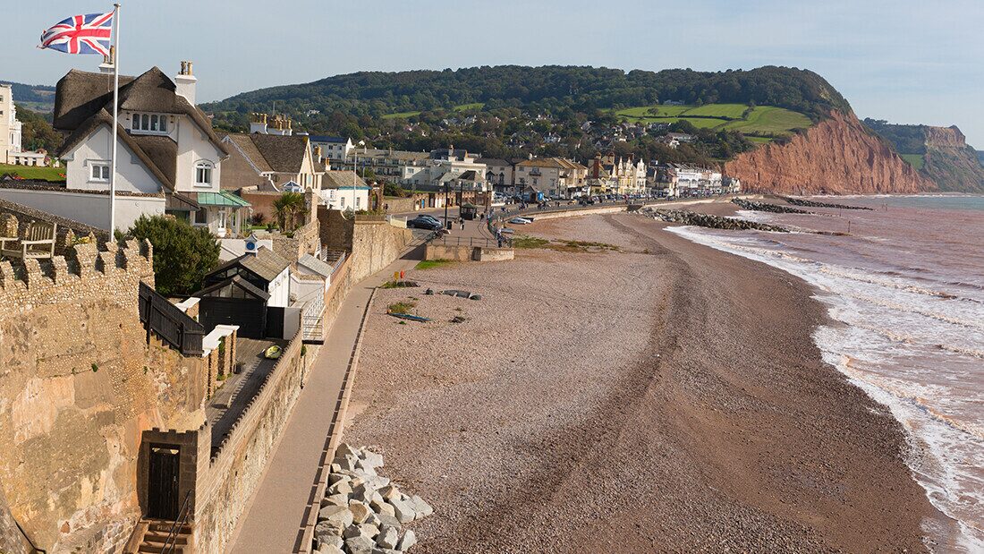 Sidmouth beach and sea front Sidmouth beach in Devon with red cliffs, pebble shoreline, seaside houses, and a Union Jack flag overlooking the coast