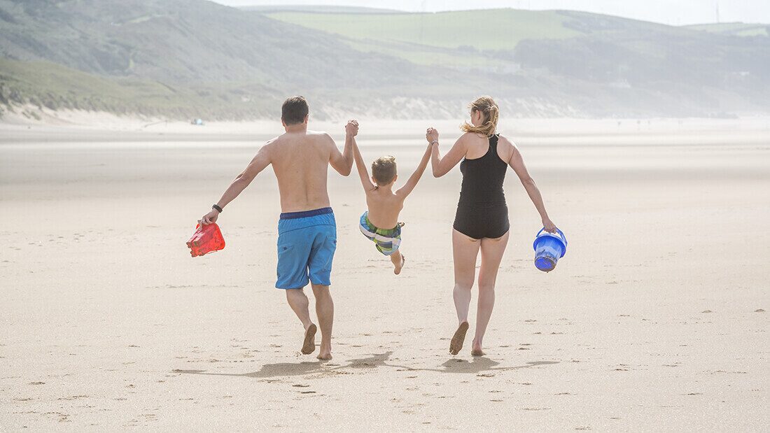 Beaches are less crowded in term time Family walking on a quiet sandy beach, parents holding child’s hands with buckets for a seaside day out.