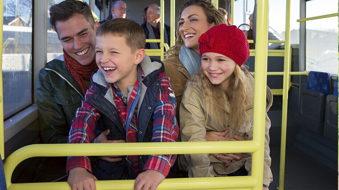 Happy family with children smiling and enjoying a bus journey together during holiday travel.
