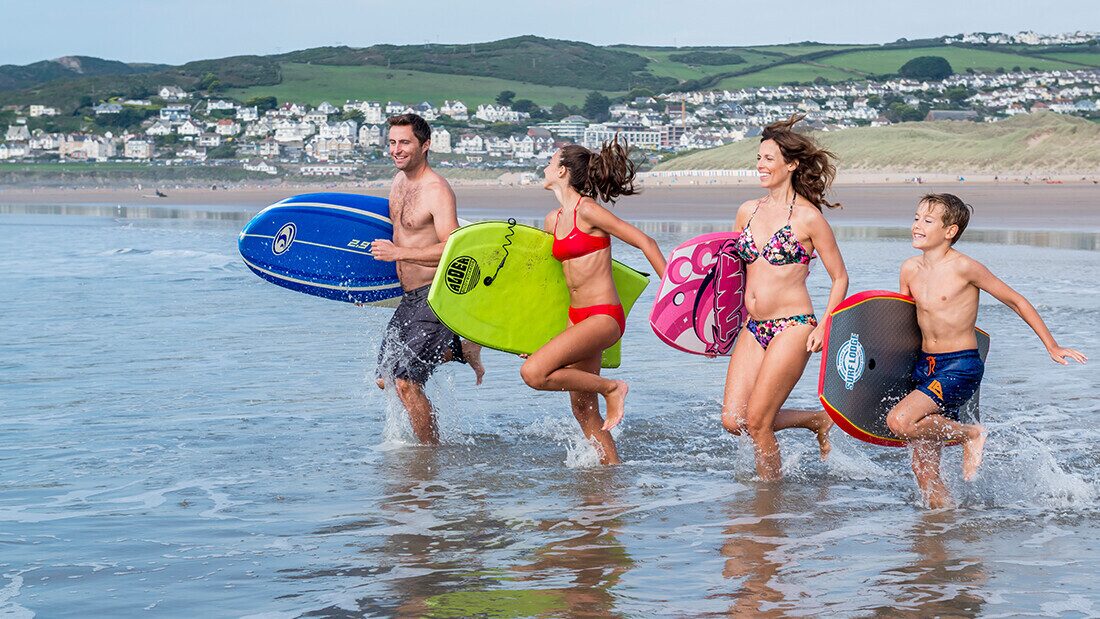 Happy family with bodyboards enjoying the sea at Woolacombe Beach in North Devon, popular UK holiday destination