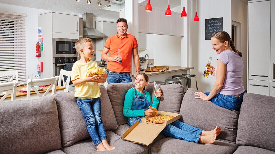 Family enjoying pizza and drinks in a self-catering holiday lodge near Woolacombe Bay, perfect for relaxed dining on Devon breaks.