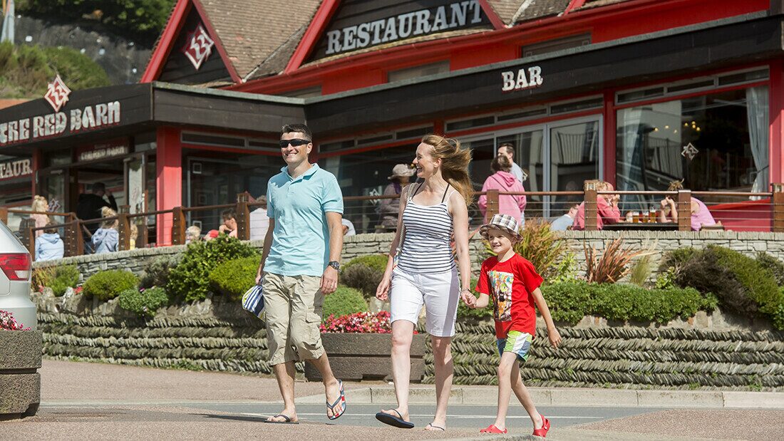 Family walking by The Barn restaurant and bar in Woolacombe, a popular dining spot for Devon holidaymakers.