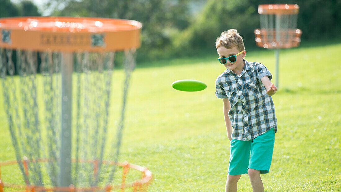 Young boy playing disc golf on a sunny holiday park field, enjoying outdoor family activities in Devon.