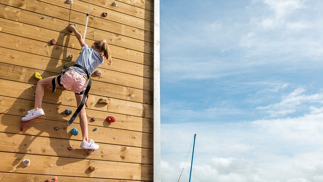 Young girl climbing an outdoor wooden climbing wall at a family holiday park adventure activity.