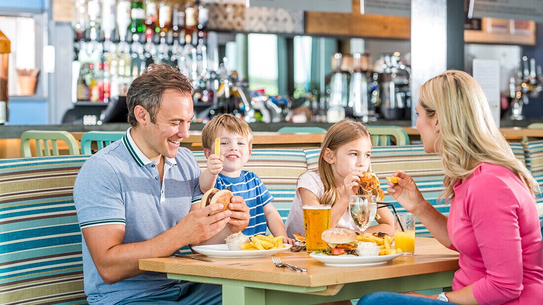 All-day café bar at Woolacombe Bay Family enjoying burgers and drinks together at the restaurant in Woolacombe Bay Holiday Parks, North Devon
