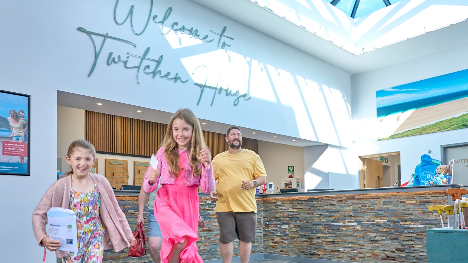 Two children and a man in holiday park reception lobby at Twitchen House, showcasing a welcoming atmosphere and modern decor.