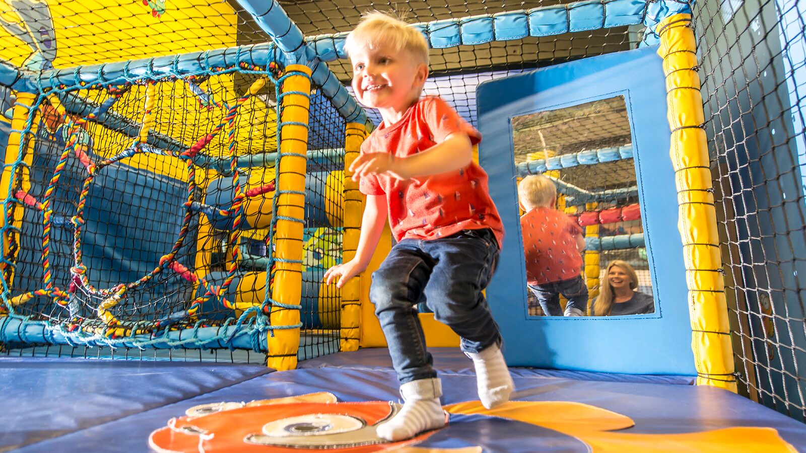 A young boy runs around in the indoor soft play area smiling as he discovers the lively environment.