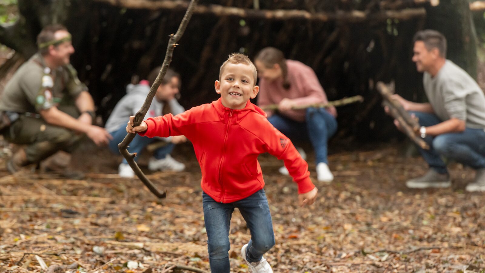 A young boy holds a branch outside a den he is building with his family at Twitchen House Holiday Park in North Devon