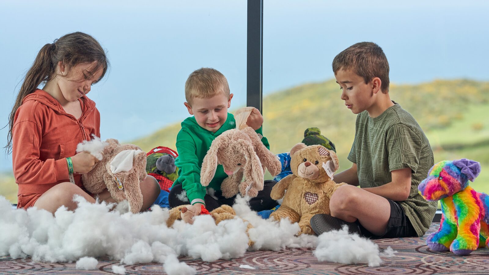 On a rug, three children happily interact with their stuffed animals, showcasing their imaginative playtime.