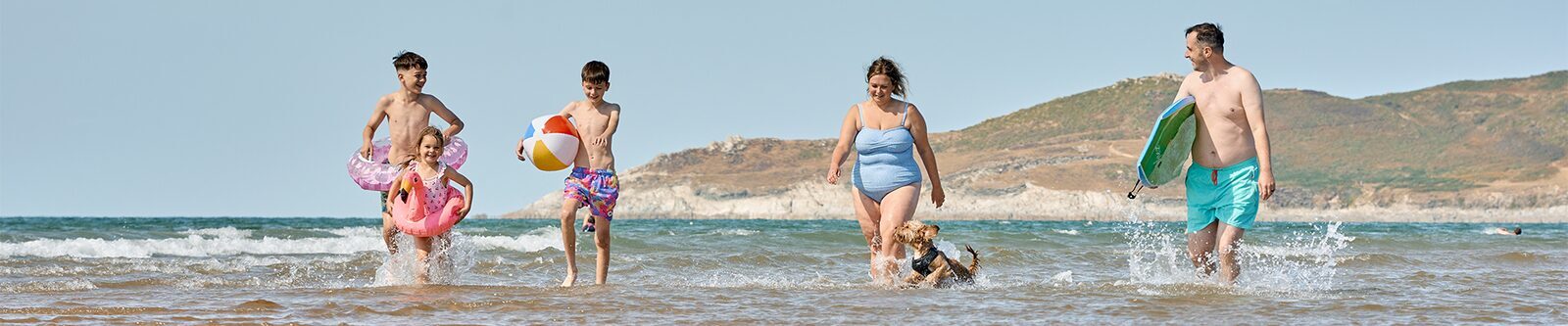 A family with their dog walking along the sandy beach in Woolacombe, enjoying the sun and ocean waves.