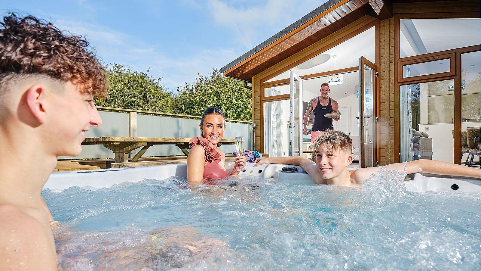 In a hot tub a woman with her two sons relax engaged in conversation by their lodge at Woolacombe Bay Holiday Park in North Devon