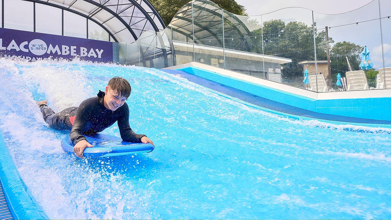 Young boy riding a body board on the Wavesurfer surfing simulator all-weather attraction at Twitchen House Holiday Park in Woolacombe, North Devon.