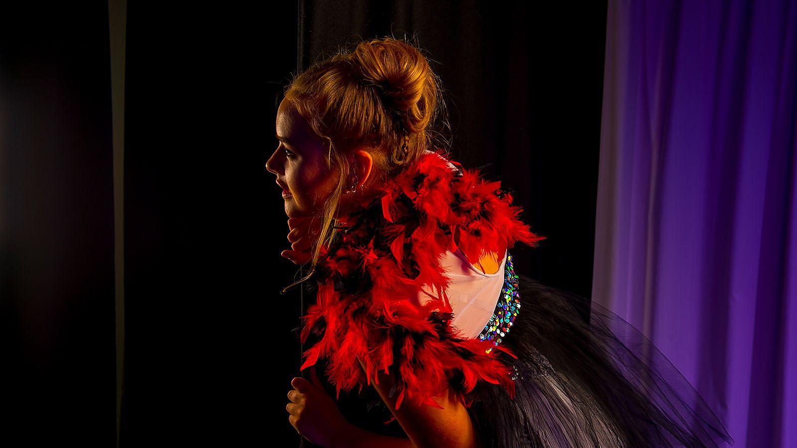 A woman in a striking red and black dress peeks confidently around the stage curtain at Woolacombe Bay Holiday Parks, showcasing her elegant style