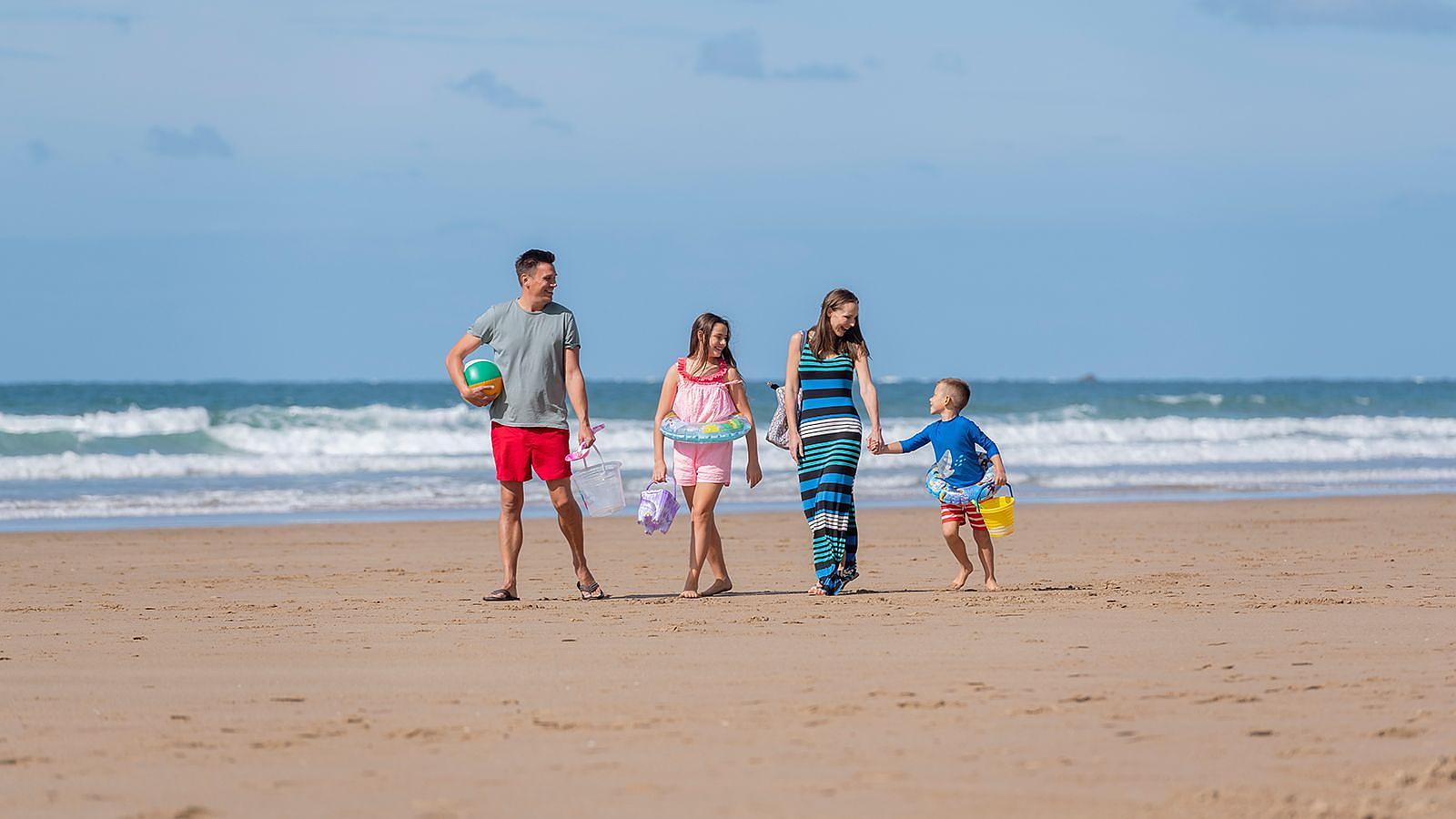 A family walks on the beach in Woolacombe, holding hands and playing with their children in the sand.