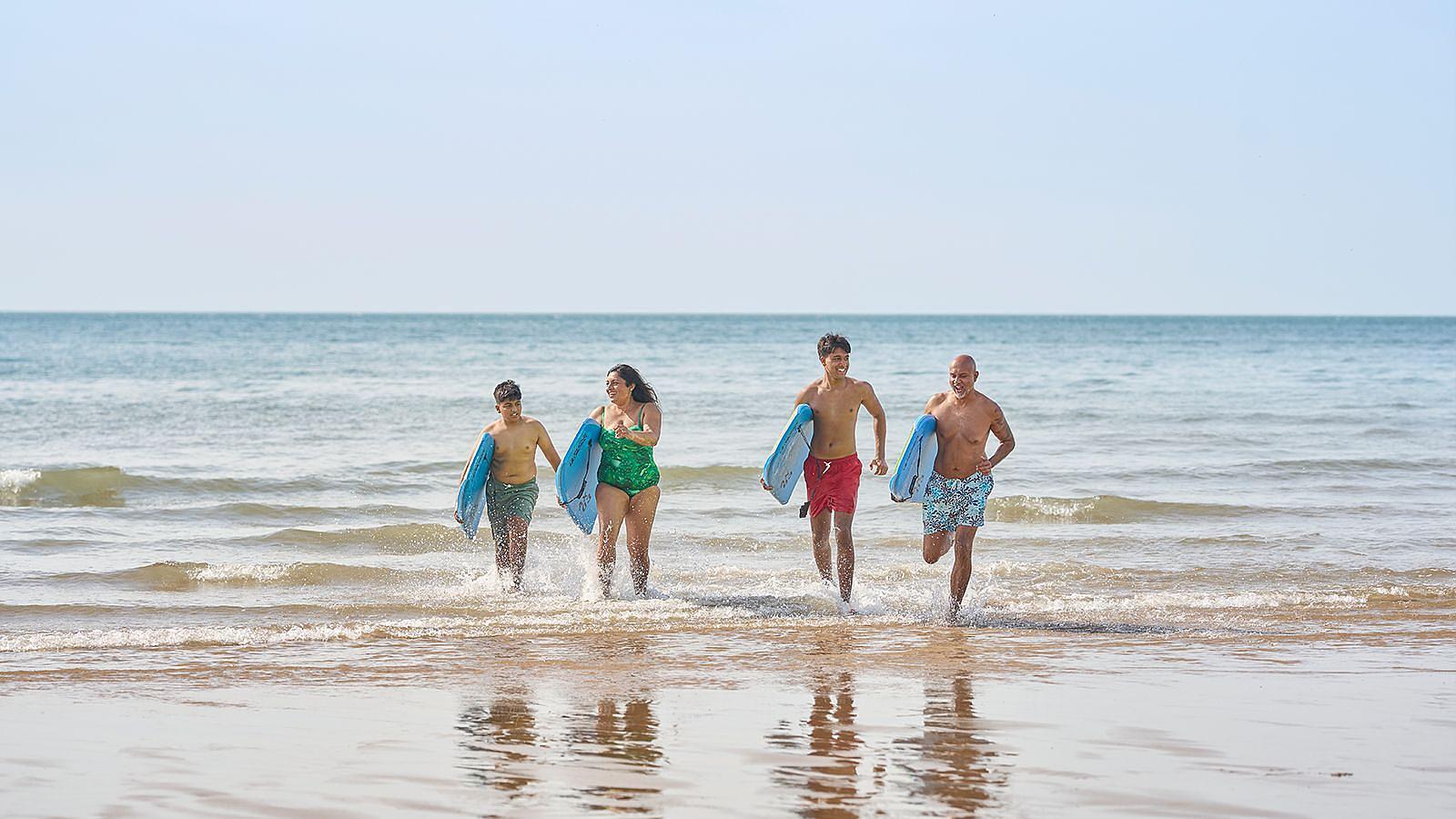 A diverse group of beachgoers walks on the sand in Woolacombe, each with a surfboard ready for surfing.