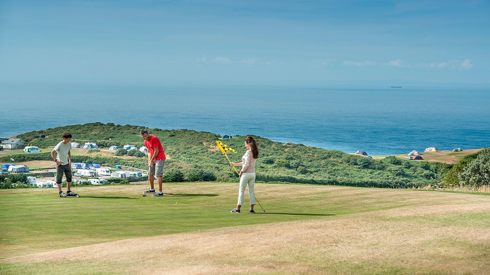 A family group of golfers on a well-maintained green field at Easewell Farm Holiday Park in Woolacombe, focused on their game.