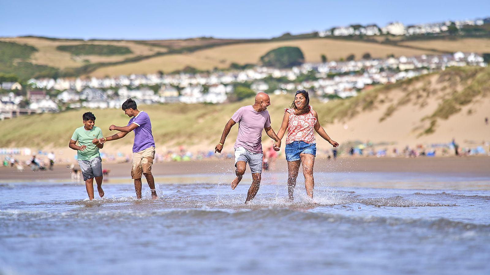 A family walk together on Woolacombe beach in North Devon on their great value cheap break at Woolacombe Bay Holiday Parks, surrounded by the beauty of the shoreline and ocean waves.