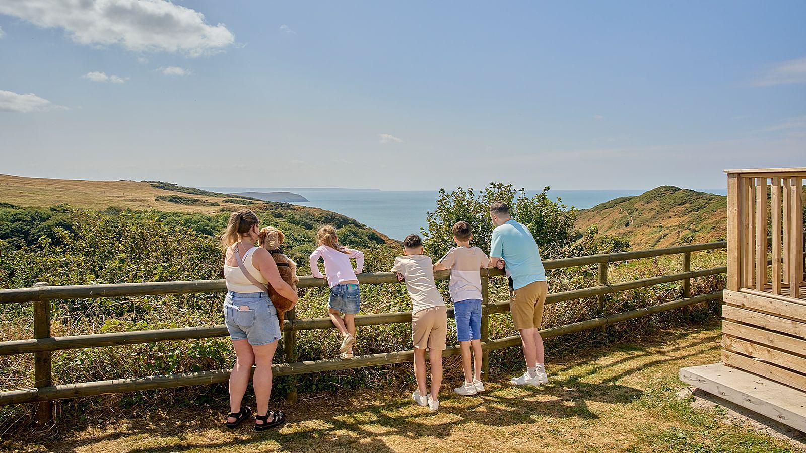 A family perched on a wooden fence, gazing at the vast ocean stretching out before them at Twitchen House Holiday Park in North Devon