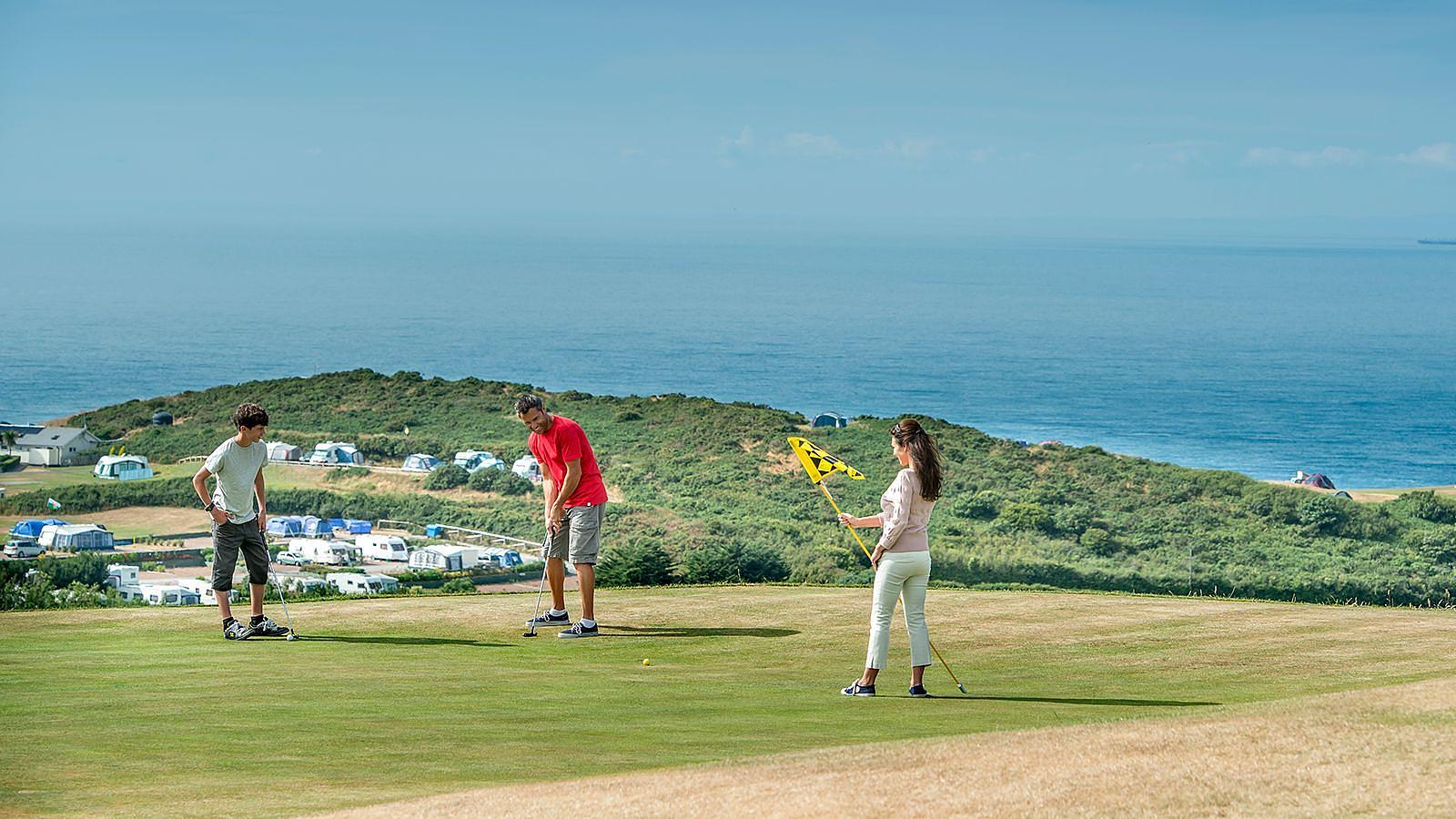 Family of three golfers enjoying a game on a vibrant green hill, surrounded by scenic views at Easewell Farm Holiday Park in Woolacombe.
