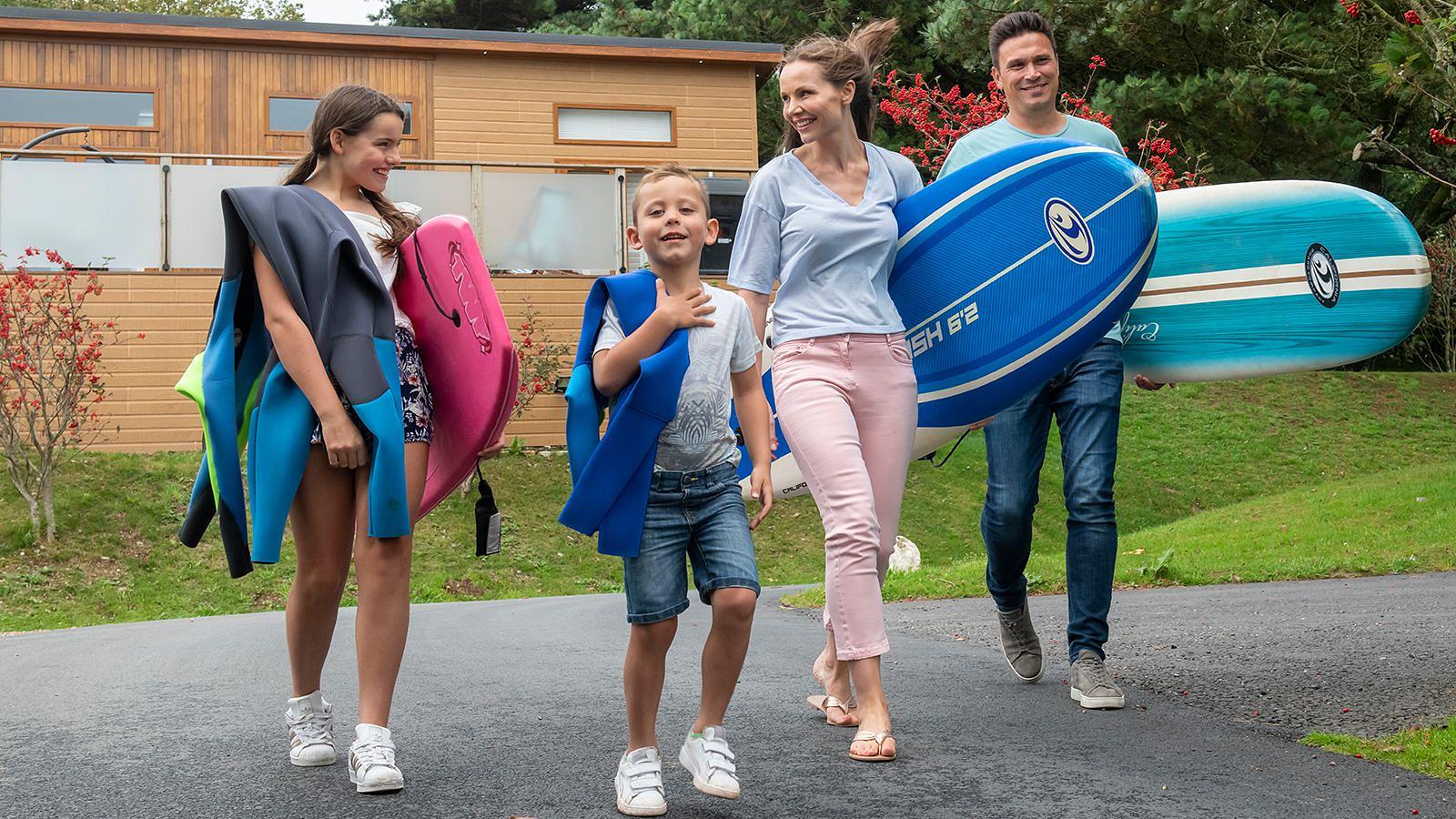 A family strolls along the road, each member holding a surfboard, ready for a day of surfing in Woolacombe.