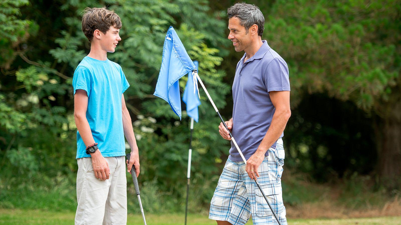 On Mortehoe & Woolacombe Golf Course, a father and son stand near flags, likely discussing strategy or enjoying a round of golf.