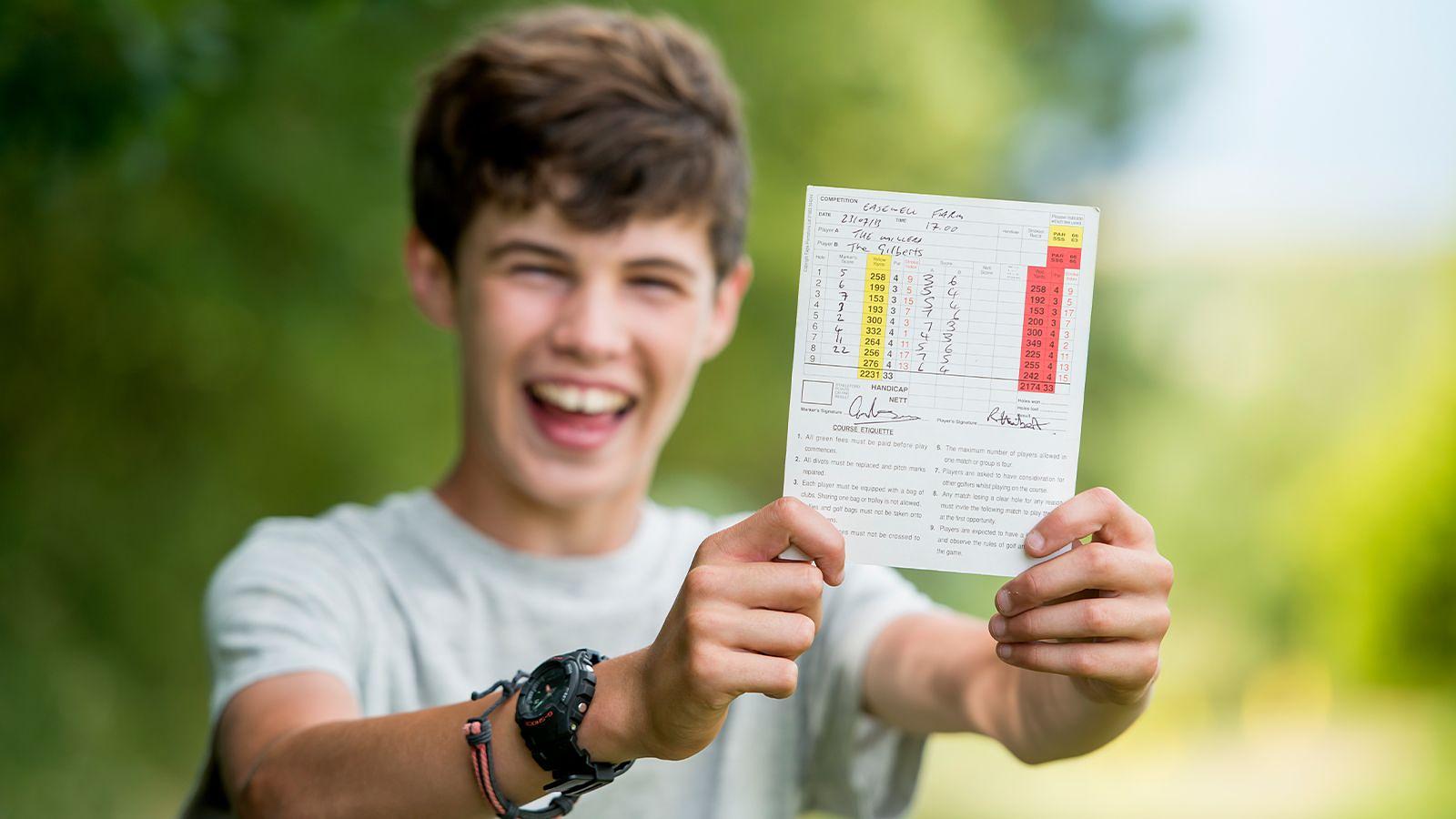 A young boy excitedly holding up his golf score card at Mortehoe & Woolacombe Golf Club in North Devon.