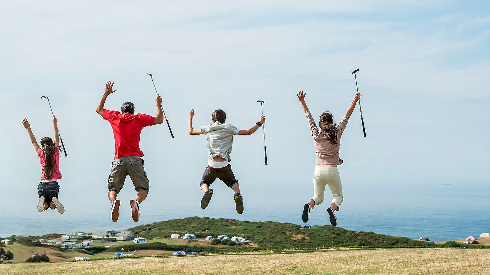 Four people enthusiastically jumping, golf clubs raised high, capturing a moment of fun and energy outdoors at Mortehoe & Woolacombe Golf Club at Easewell Farm.