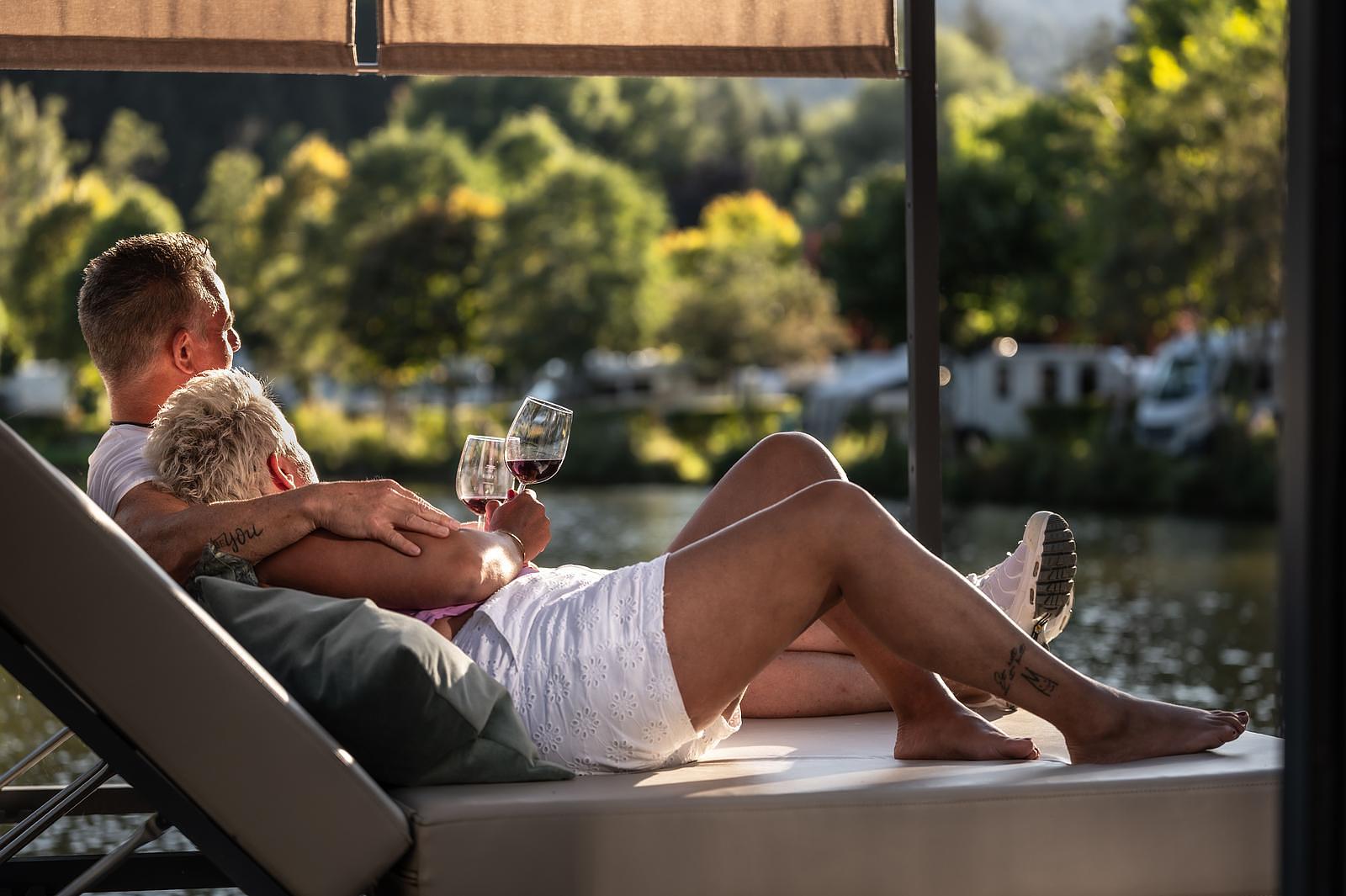 Verliebtes Pärchen entspannt bei einem Glas Wein auf der Sonnenliege des Floating Homes im Ferienparadies Natterer See