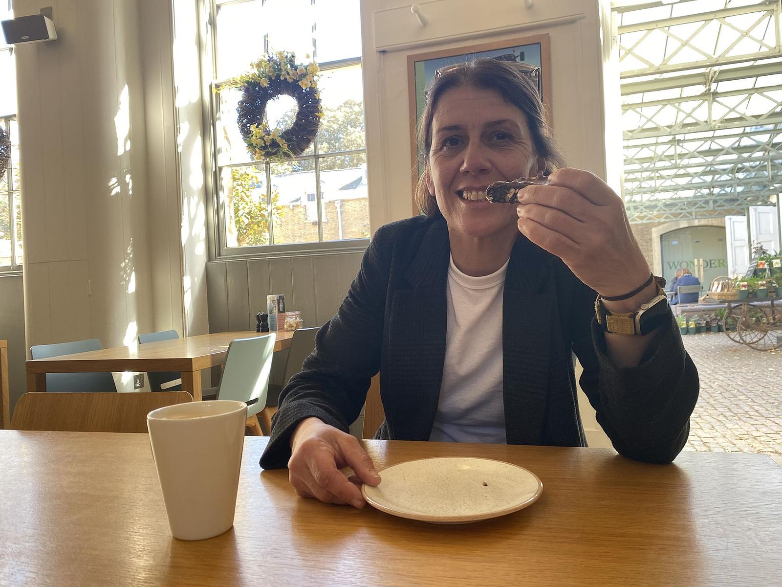 A lady sits at a wooden table holding a piece of cake.
