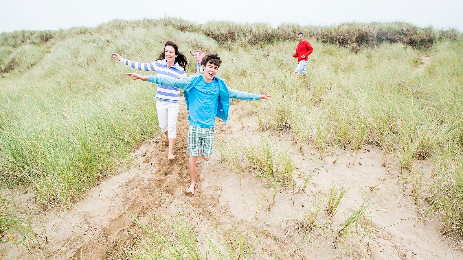 A family of four navigating the undulating sand dunes in Woolacombe on a sunny spring day.