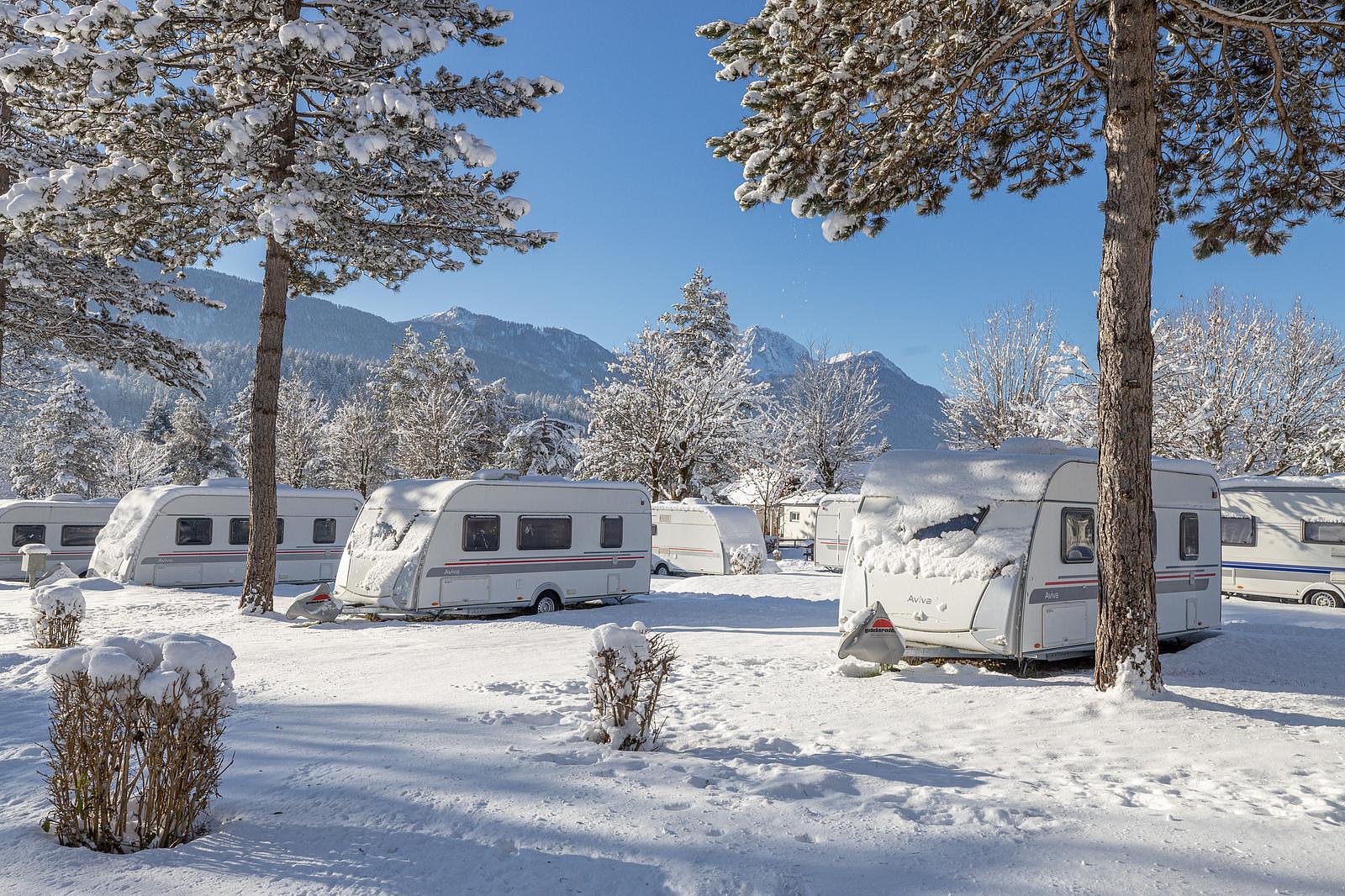 Campingplatz im Schnee mit Wohnwagen und Bergen