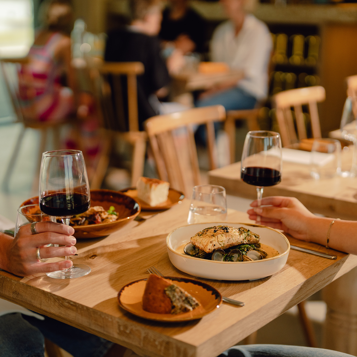 Diners enjoying a meal at Firefly Restaurant, with glasses of red wine and seasonal dishes served on a wooden table in a relaxed restaurant setting.