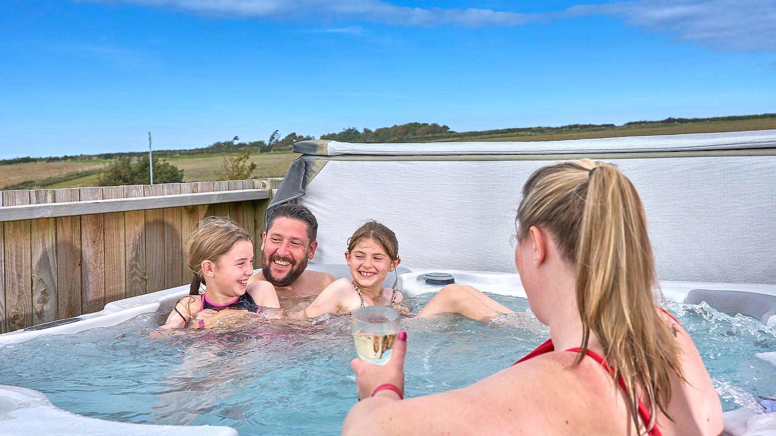 A family enjoys a sunny day in a hot tub, laughing and relaxing together in a warm, inviting atmosphere at Twitchen House Holiday Park in Woolacombe.