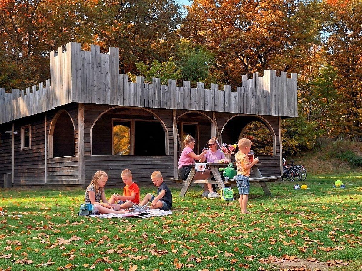 Familie picknickt in der Herbstsonne vor einer Burg-Lodge im Ferienpark Drouwenerzand