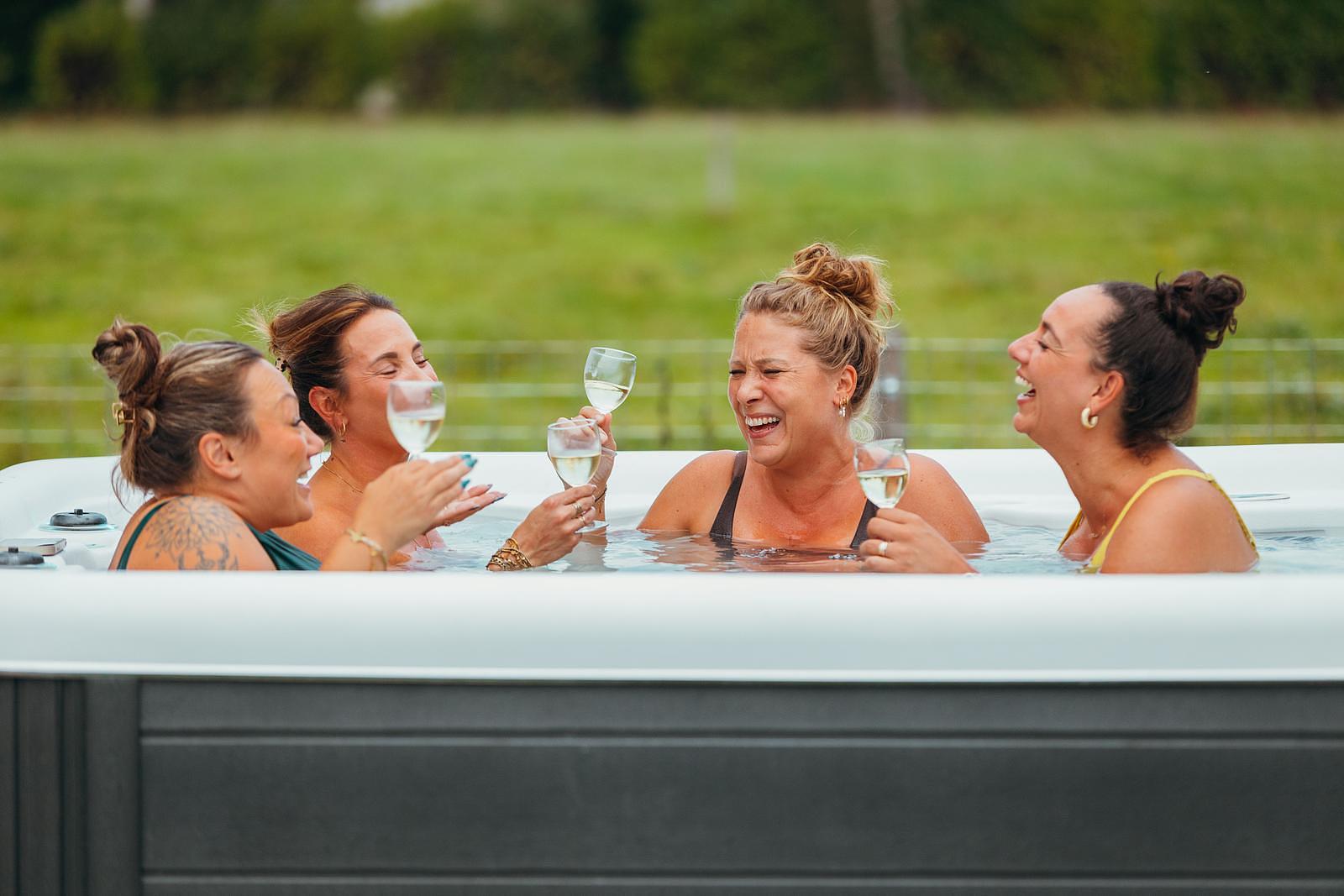 Eine Gruppe von Freundinnen sitzt gemeinsam mit je einem Glas Sekt in der Hand im Hot Tub, alle lachen herzlich