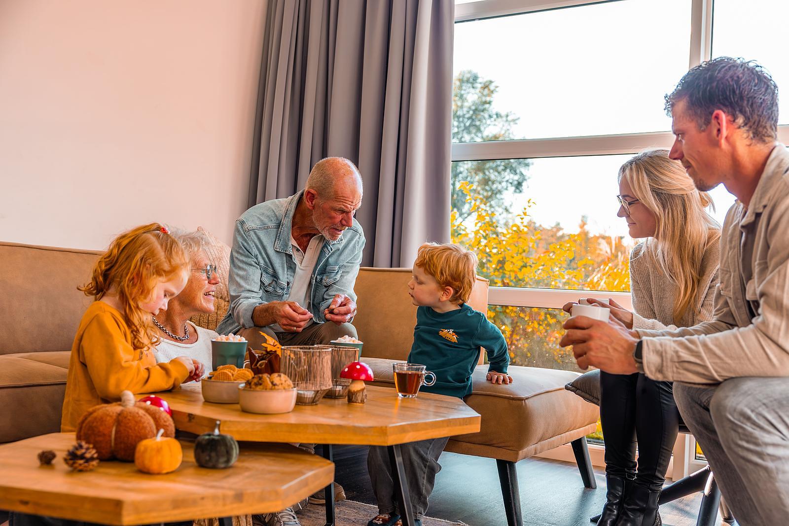 Family with grandparents and children sitting together in the bright living room of a holiday home