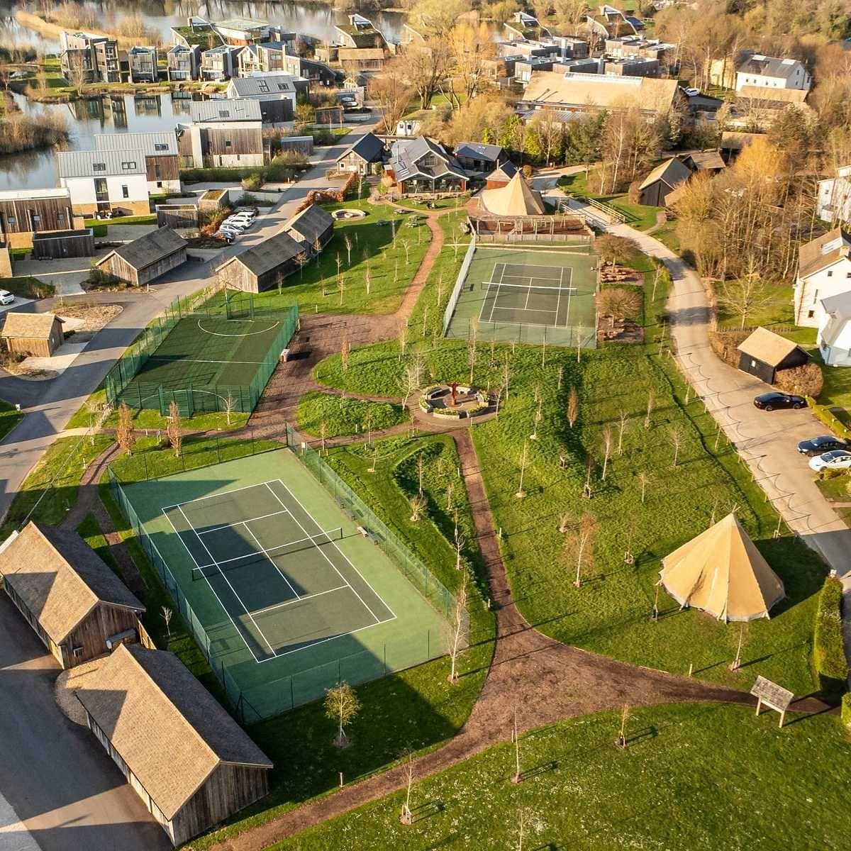 Aerial view of on-site sports facilities and holiday homes at Lower Mill Estate, surrounded by lakes and green spaces.